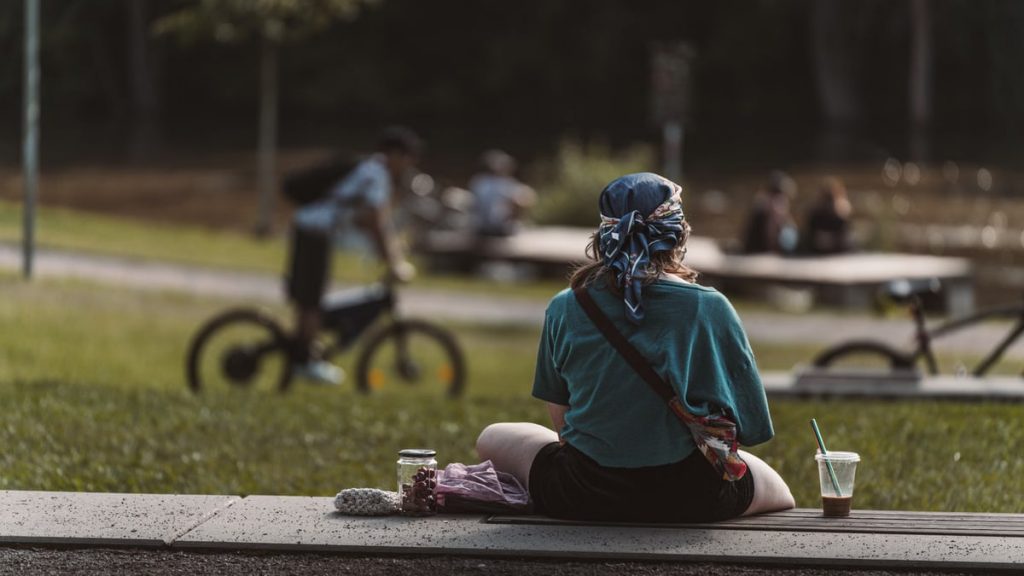 A woman sitting alone in a sunny park in Graz, Austria, enjoying leisure time with iced coffee.