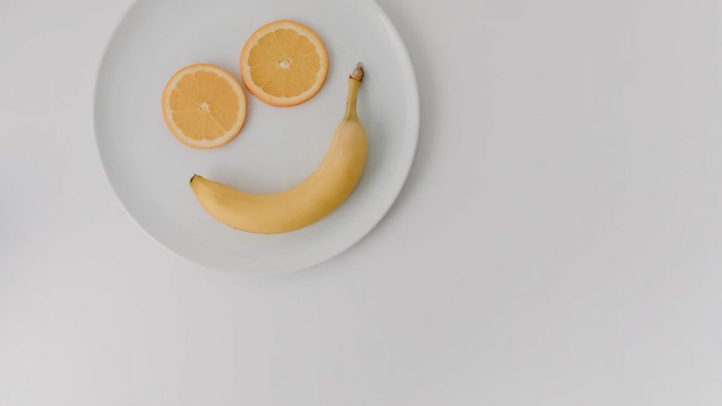 A playful arrangement of banana and orange slices forming a smile on a white plate.