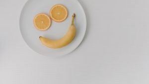 A playful arrangement of banana and orange slices forming a smile on a white plate.