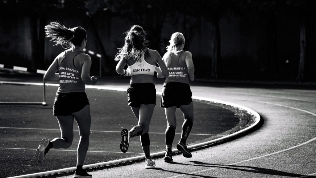 Black and white back view of unrecognizable fit female runners in sportswear running during track and field competition