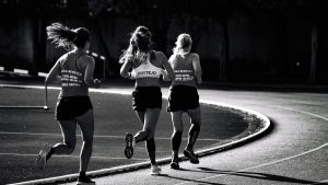 Black and white back view of unrecognizable fit female runners in sportswear running during track and field competition