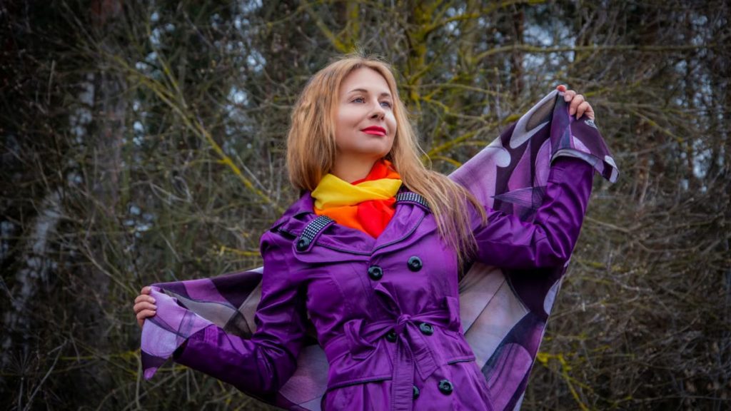 Stylish woman in vibrant purple coat and scarf enjoying a crisp autumn day outdoors.